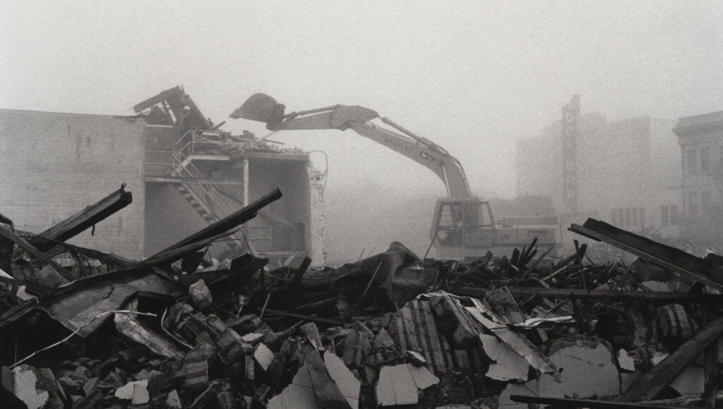 Rubble of a collapsed building, with excavator in the background, in downtown Santa Cruz