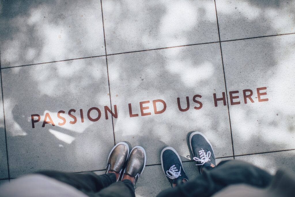 Picture of the text "Passion led us here" on a sidewalk, with feet